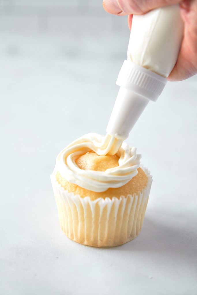 using a piping bag to pipe vegan vanilla frosting onto cupcakes