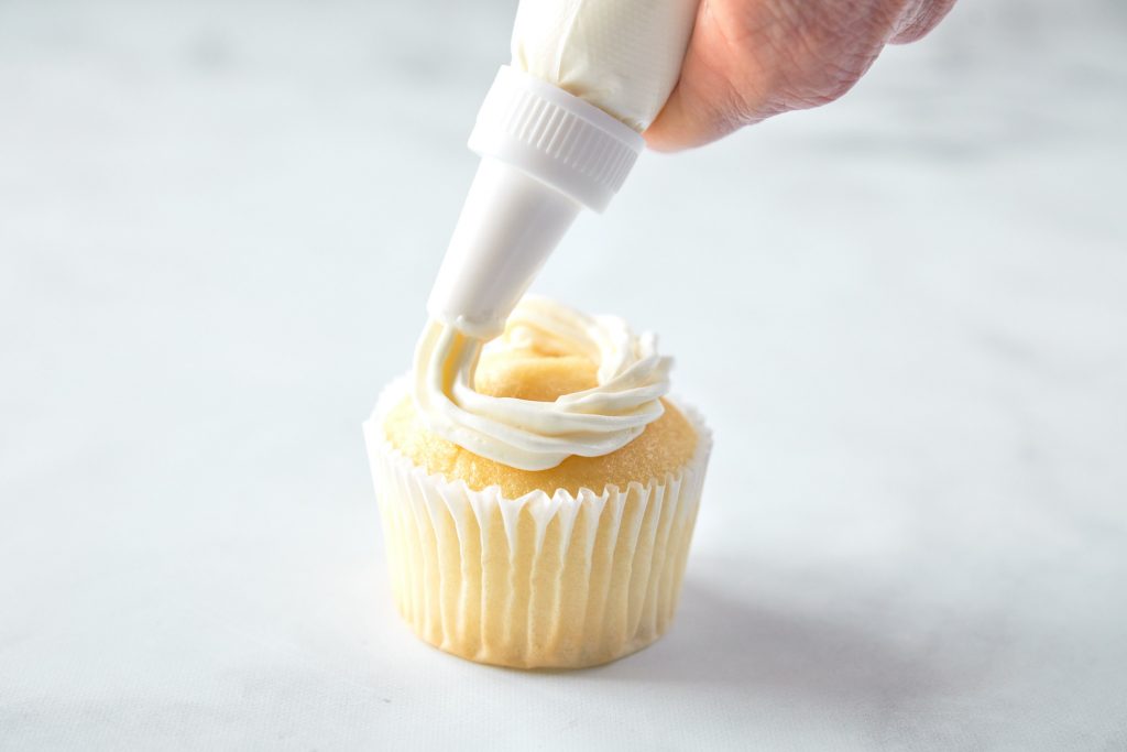 piping vegan vanilla frosting onto a cupcake