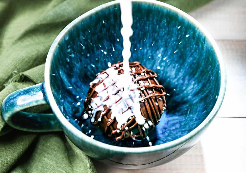 milk being poured over hot chocolate bombs in a blue mug