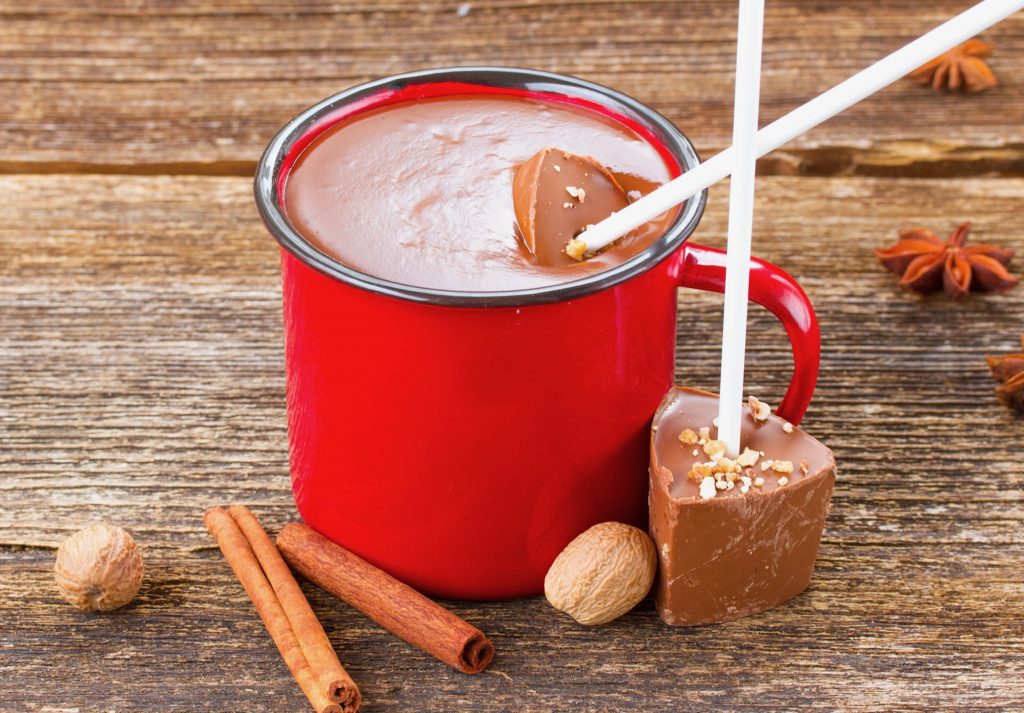 hot chocolate sticks lying next to a cup of hot chocolate in a red mug