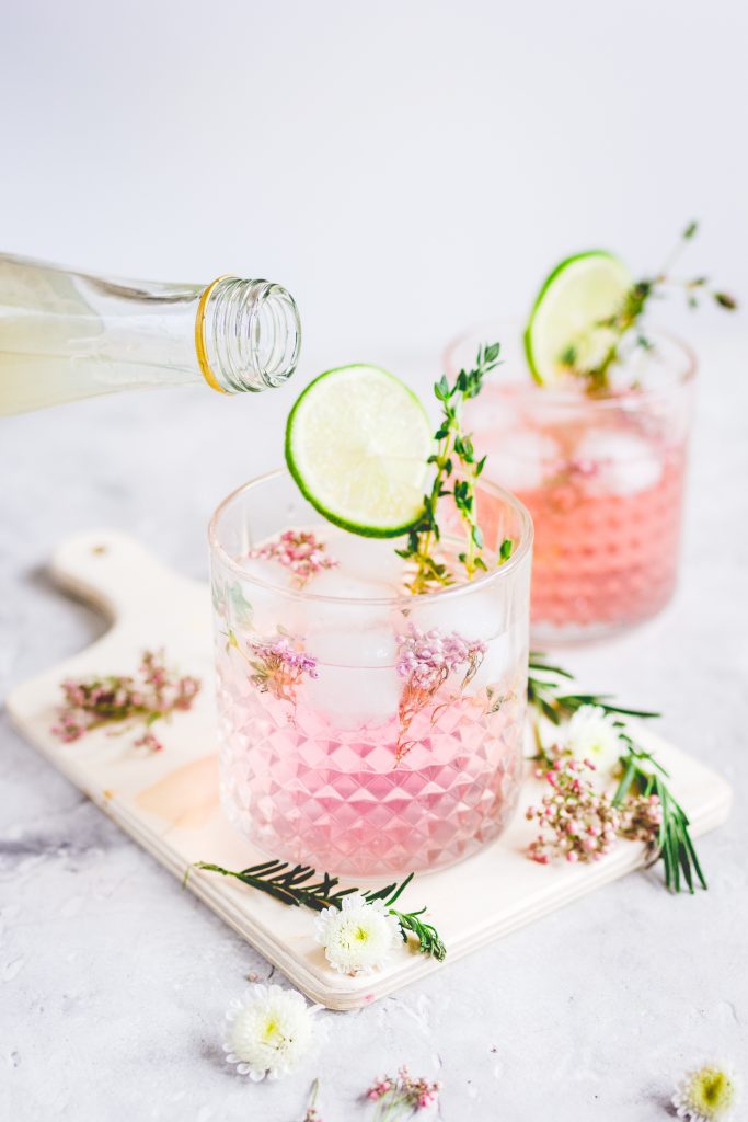 pouring liquid into pink vodka lemonade garnished with flowers