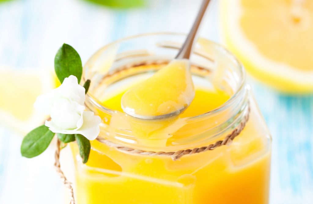 close up of eggless lemon curd on a spoon with a small jar