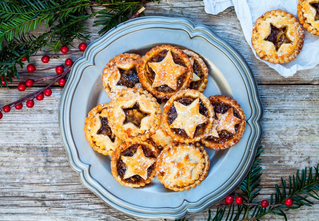 tiny vegan mince pies with stars cut out of them on a blue plate with red berries around 