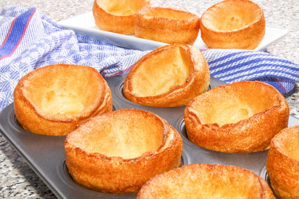 vegan yorkshire puddings in a muffin tin after baking with a blue dish towel