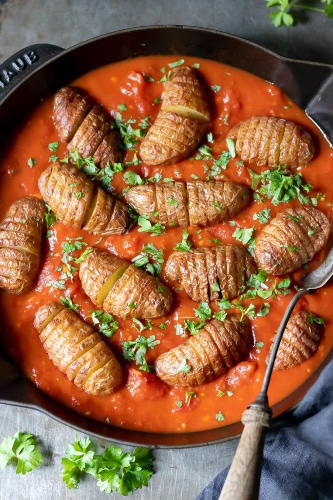 Photo of Baby Hasselback Potatoes being served in a cast iron pan with harissa-spiced tomatoes.