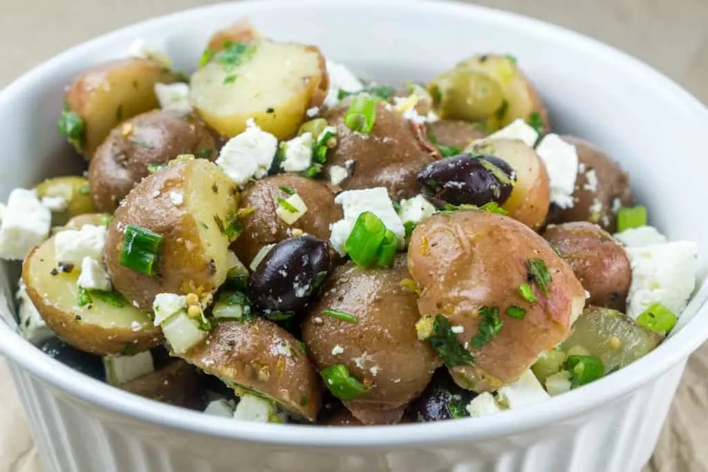 Photo of No Mayo Potato Salad With Feta & Olives being served in a white bowl.