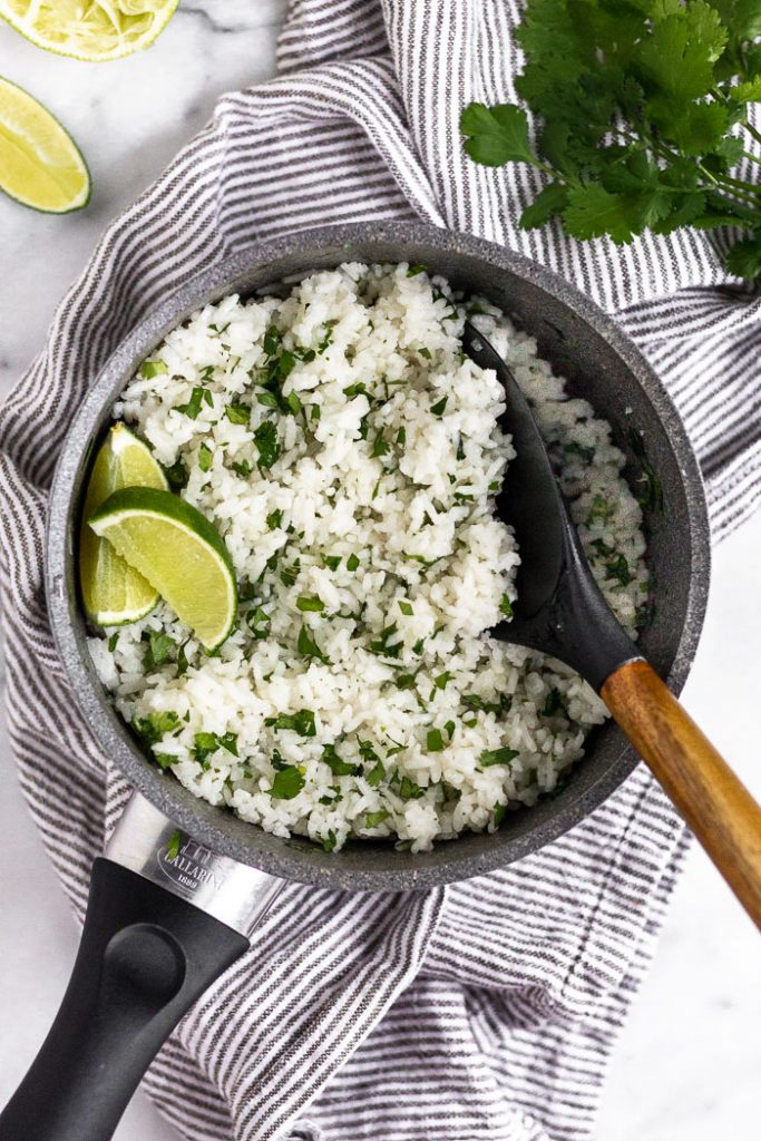 Photo of cilantro lime rice being served from a pot with a wooden spoon.