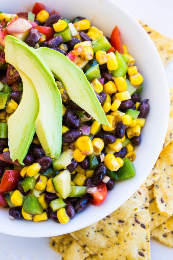 Photo of Spicy Cowboy Caviar being served in a round white round bowl with avocado slices on top.