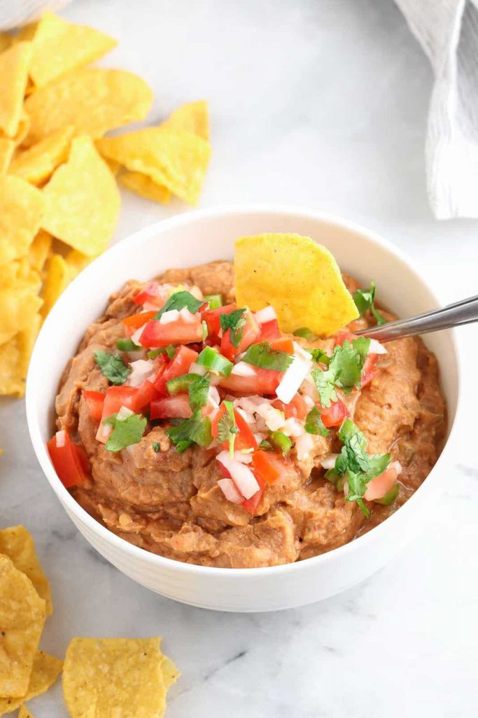 Photo of vegan refried dean dip being served in a small round white bowl with chips.