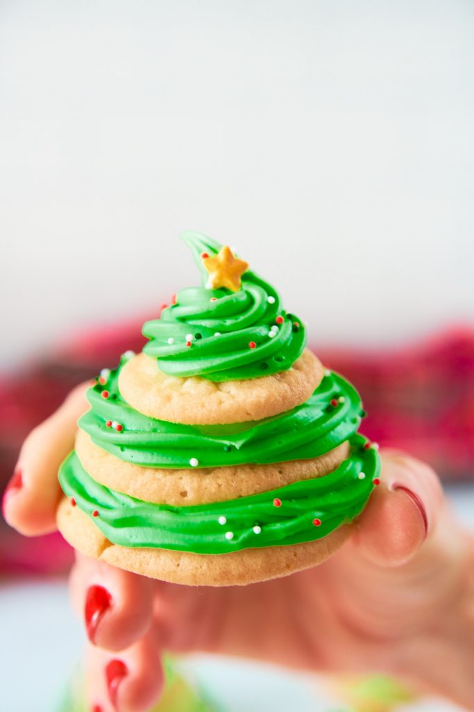 hand holding a stacked sugar cookie Christmas tree cookie with green icing