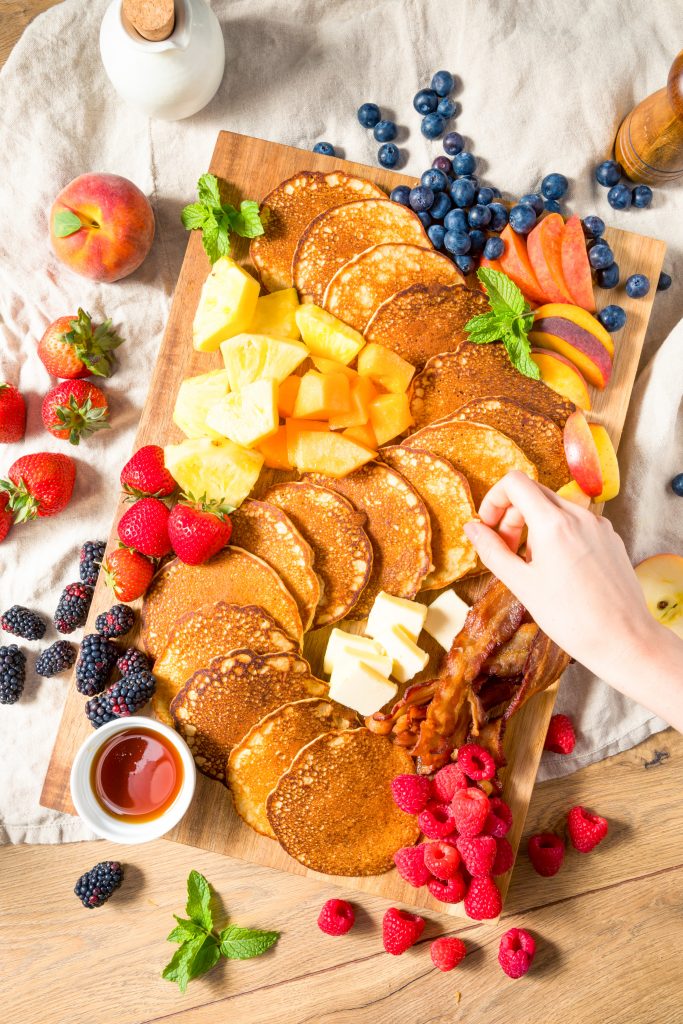 hand reaching for pancakes on a breakfast or brunch board with fruit