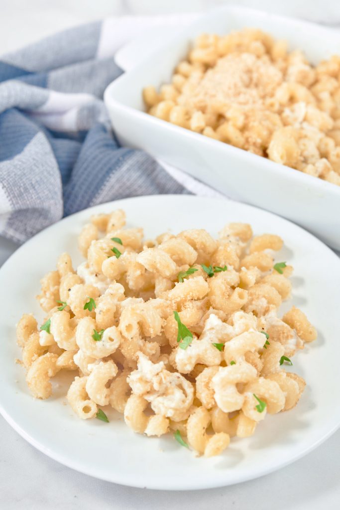 White plate with brie mac and cheese on it and dish in the background with parsley 