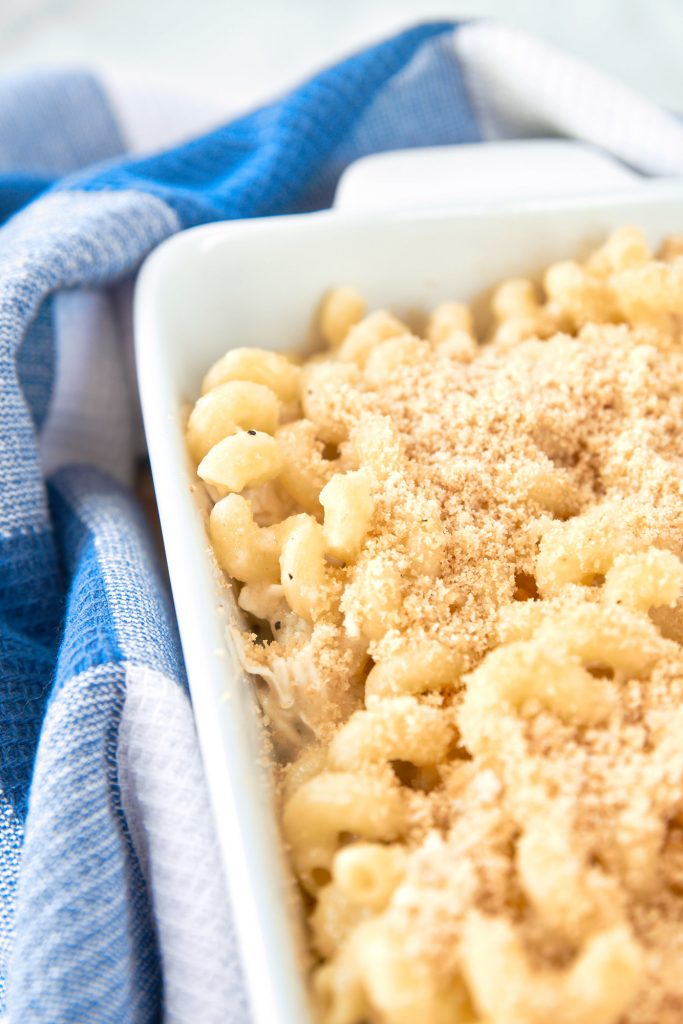 Close up of side of a dish with baked brie mac and cheese with breadcrumbs in it with blue dish towel in the background