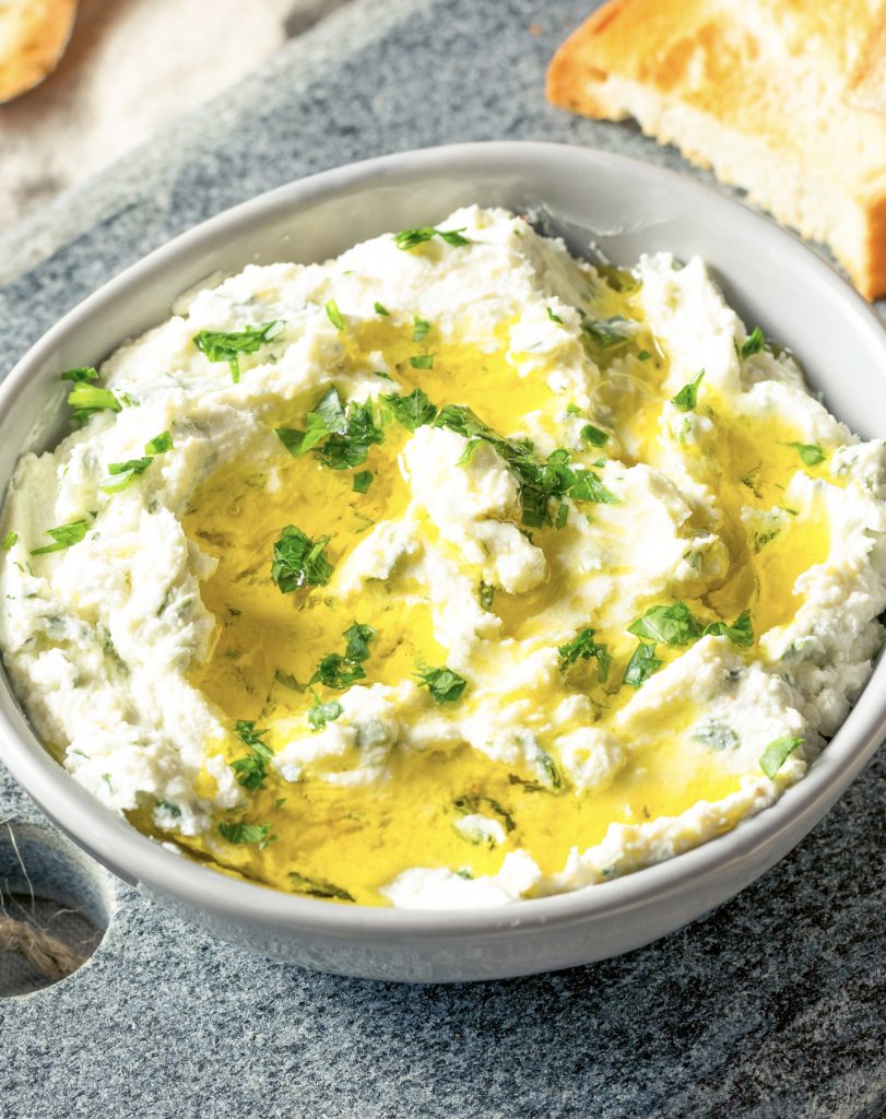 Grey bowl of herb goat cheese dip with olive oil