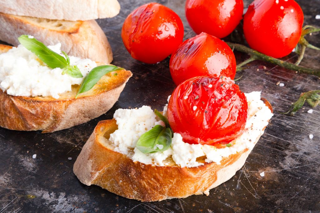goat cheese dip spread on a crusty piece of bread with a tomato.