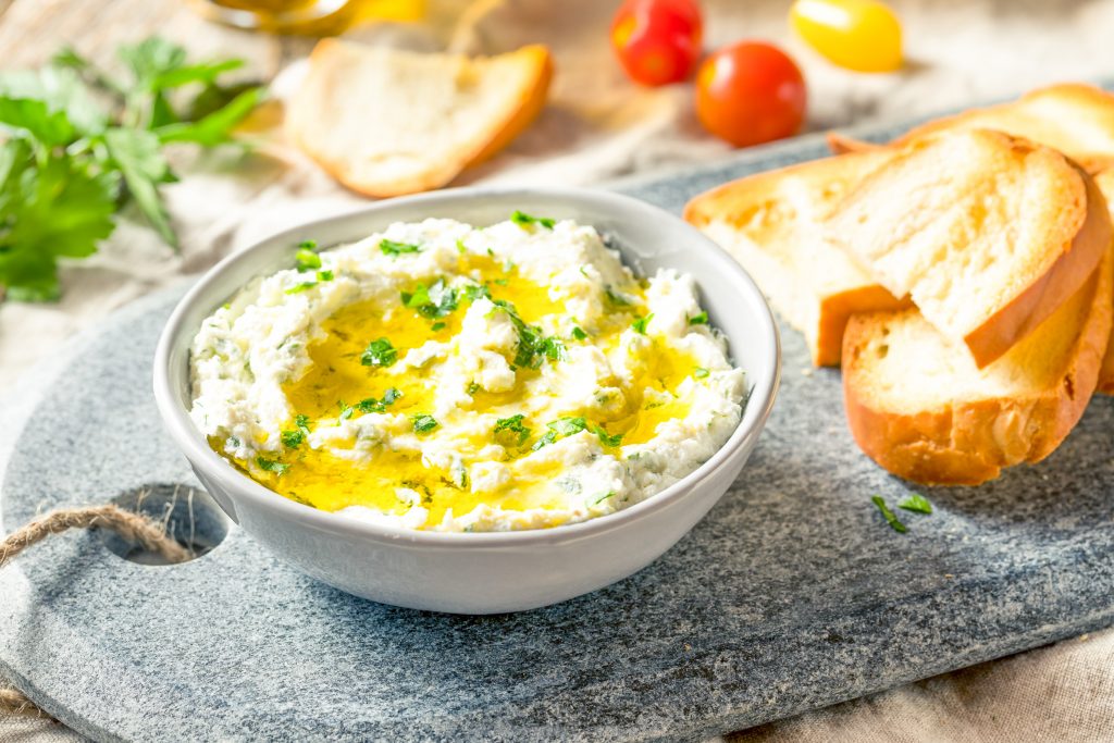 freshly whipped goat cheese dip with herbs in a bowl for serving next to bread.
