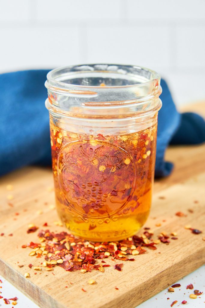 Jar with a hot honey recipe on a wooden cutting board with red pepper flakes.