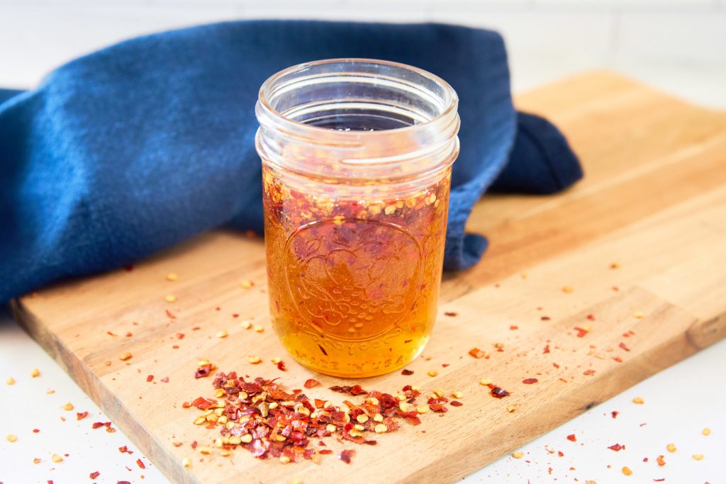 hot honey recipe in a jar with chili flakes on cutting board
