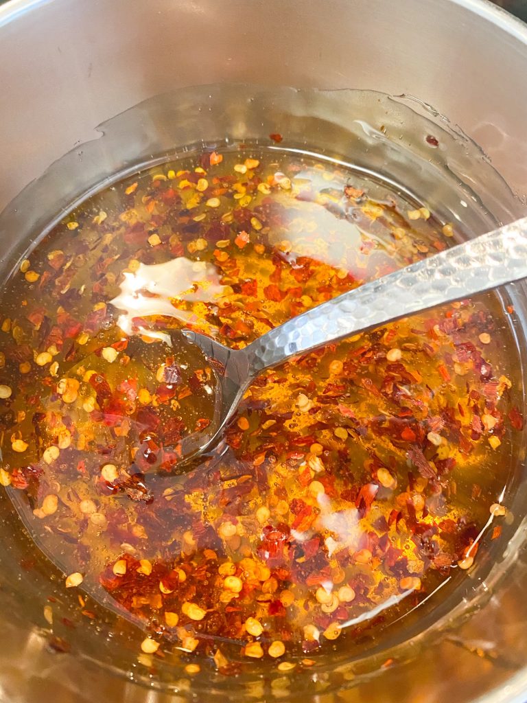 Spoon mixing chili and hot sauce in honey on the stove.