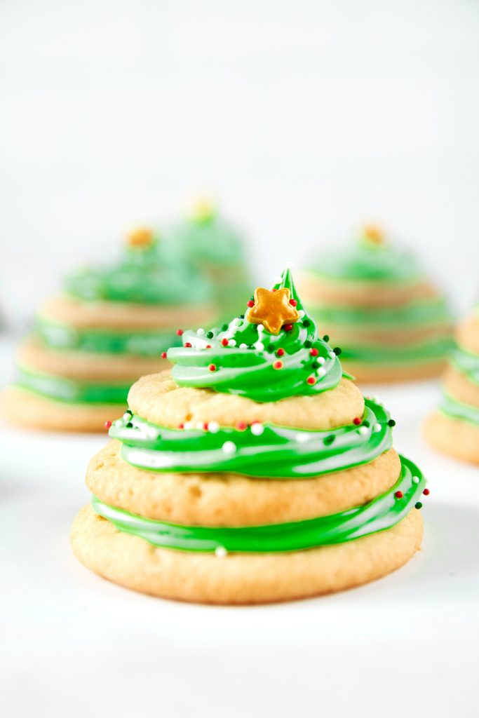 close up of the stacked sugar cookie Christmas tree cookies with green icing and a gold star and other cookies in the background 