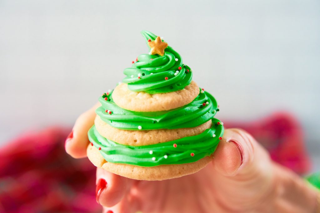 hand holding a stacked sugar cookie Christmas tree with red cloth in the background