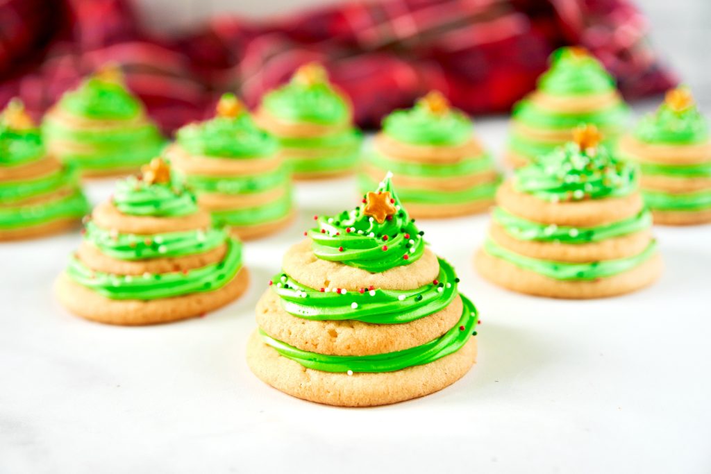 many stacked sugar cookie christmas trees with green icing on a white counter