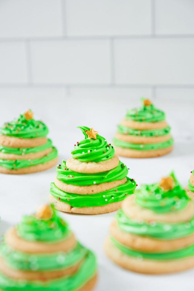 multiple stacked sugar cookie Christmas trees on a tray with green icing and gold star decorations