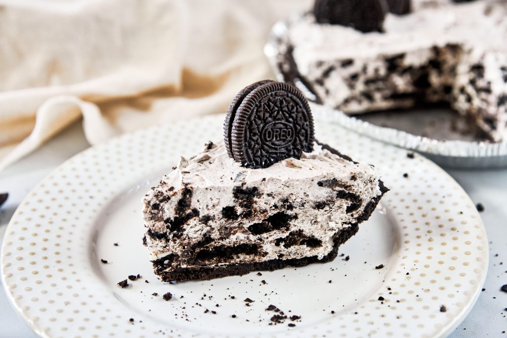 slice of vegan Oreo cheesecake with cut cake in the background