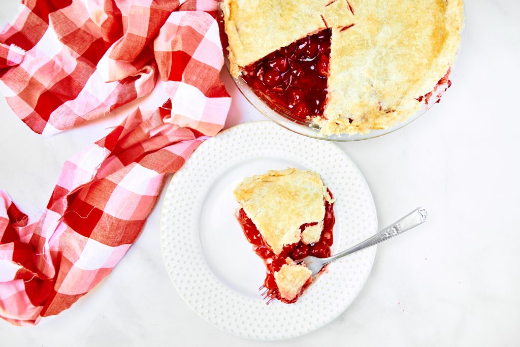 slice of vegan cherry pie taken out of the pie which is in the background