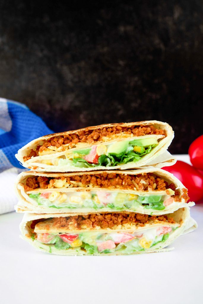 three vegan crunchwrap supremes stacked on a white counter and black background