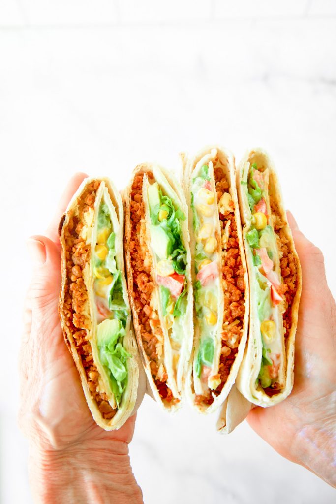 vegan crunchwrap supreme being held between hands