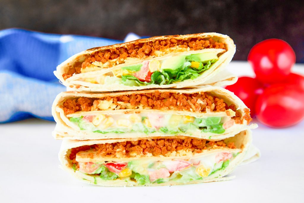 three vegan crunchwrap supreme Tacobell copycat recipe stacked on top of each other with tomatoes in the background