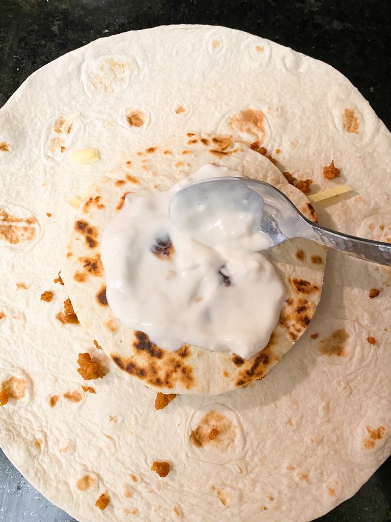 spreading sour cream on top of a tortilla