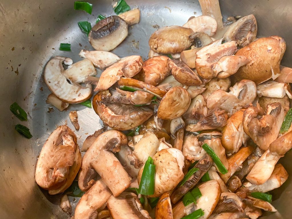 Funghi e cipolle verdi in cottura in una pentola