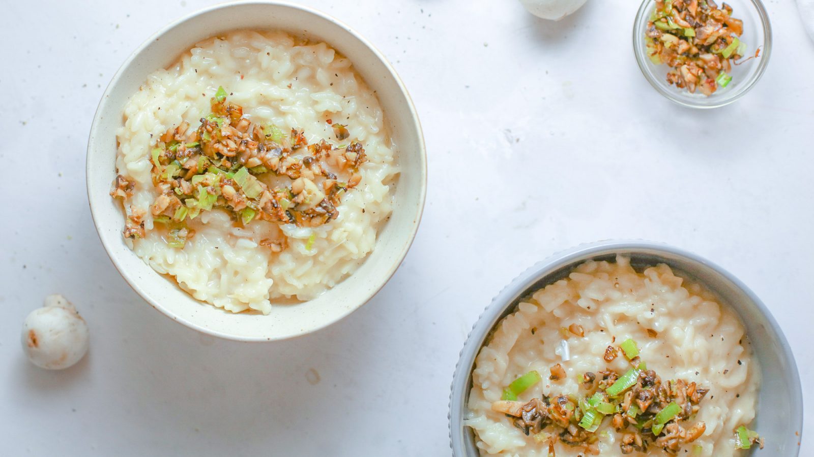 vegan mushroom risotto in two bowls topped with leeks and walnuts