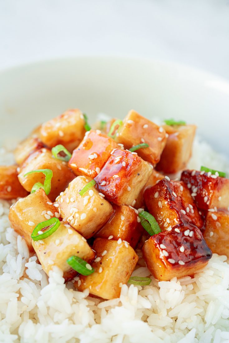 vegan orange tofu in a bowl with rice and green onions