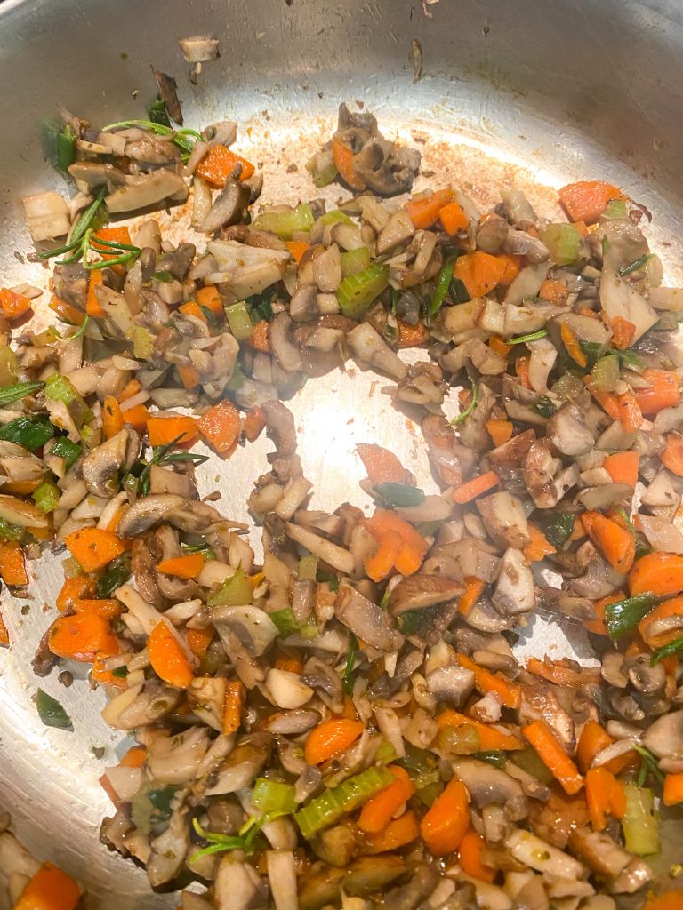 Chopped carrots, mushrooms, and green onions sauteing in a pan with the liquid gone.