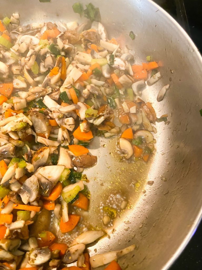 Chopped carrots, mushrooms, and green onions sauteing in a pan with liquid from the mushrooms.