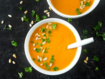 vegan carrot ginger soup portioned into two bowls on black background