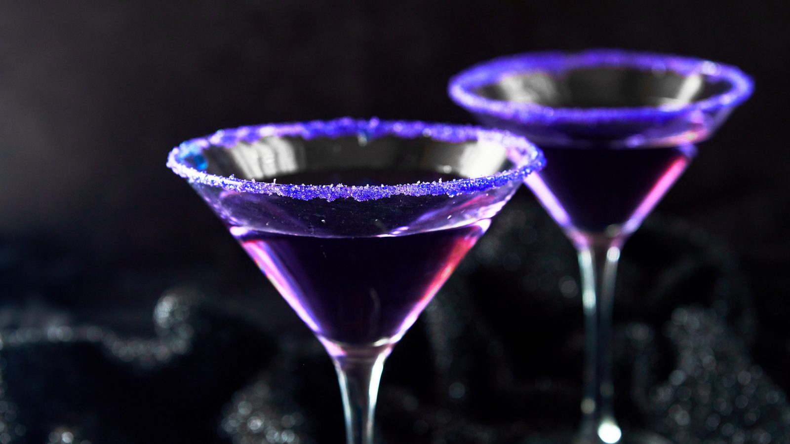 two purple Halloween cocktails on a black background
