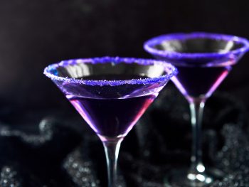 two purple Halloween cocktails on a black background
