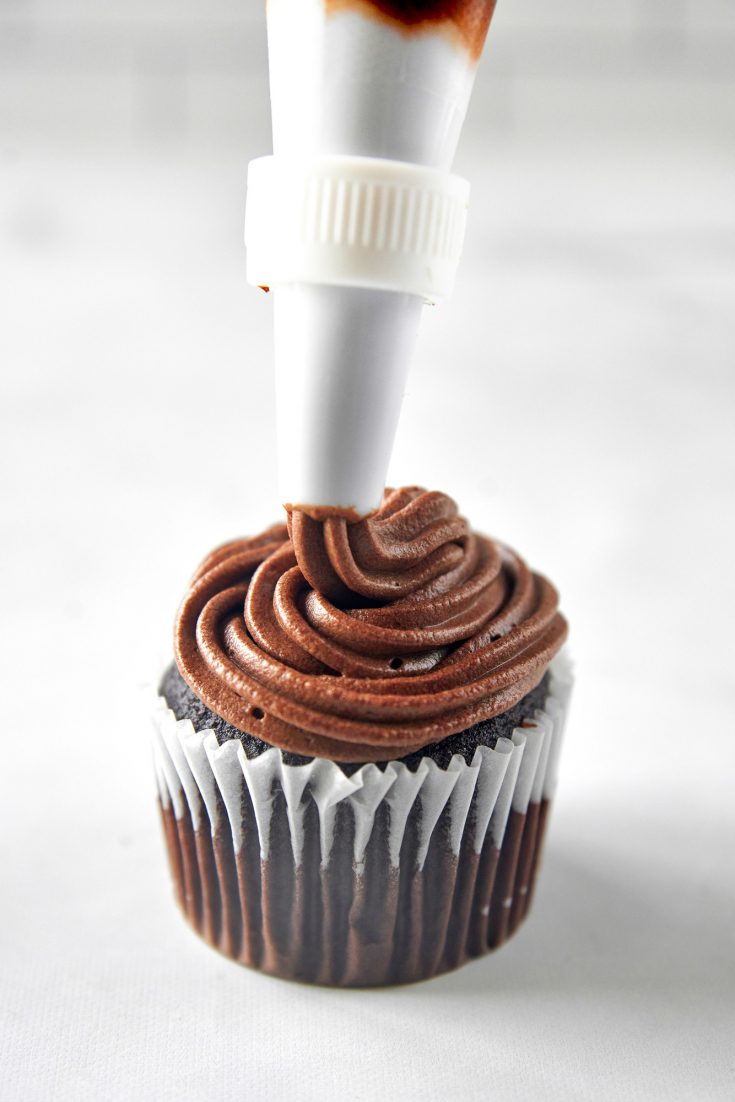 piping vegan chocolate frosting onto a cupcake