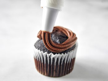 vegan chocolate frosting being piped onto a cupcake