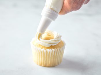 using a piping bag to pipe vegan vanilla frosting onto a cupcake