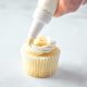 using a piping bag to pipe vegan vanilla frosting onto a cupcake