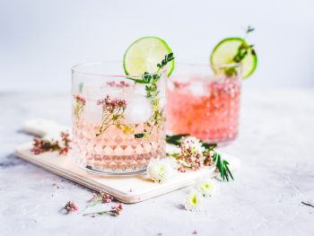 pink vodka lemonade in two cups garnished with limes and flowers