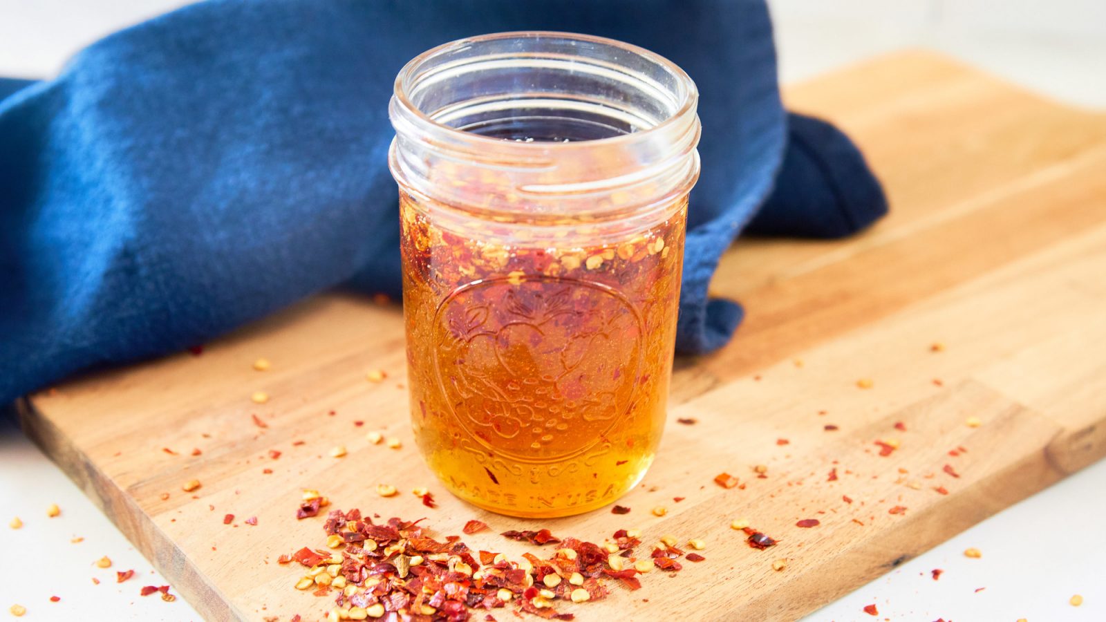 jar filled with a hot honey recipe on cutting board with red pepper flakes