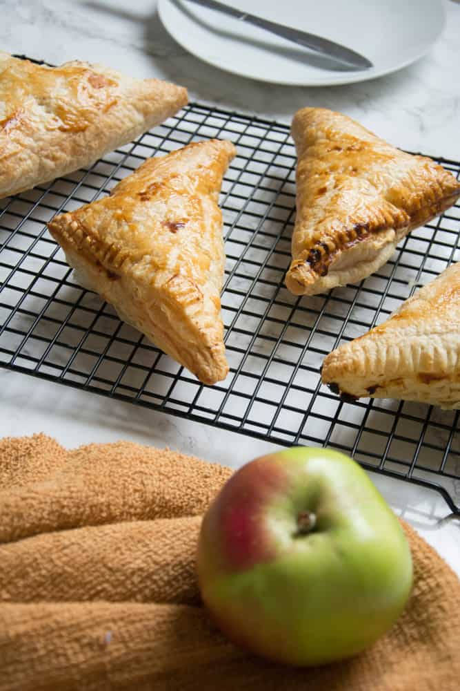 vegan turnovers sitting on a cooling rack with white plate with knife and green apple