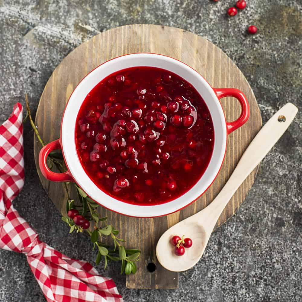 cranberries in a red bowl with a spoon and towel around them