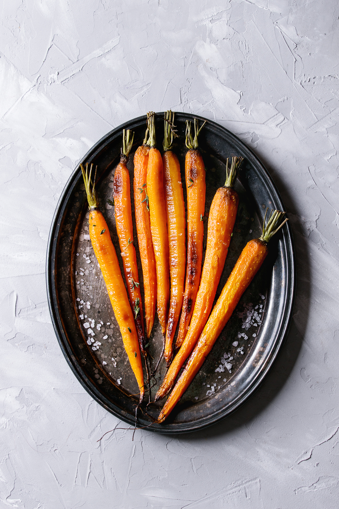 multiple orange vegan glazed carrots on a black plate with tops still on